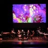 Orchestra performing with brain waves visualized on screen above.