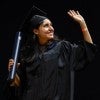 A graduating woman waves after accepting her diploma. 