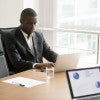 African American man sits at computer at a conference room table.