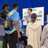 A male Asian graduate student stands in front of a poster, explaining science to a diverse group of kids