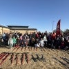 A group of people standing outside on a sunny day. A row of shovels and tools is laid out on the ground in front of them.