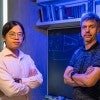 two researchers face the camera with arms crossed in front of a blackboard