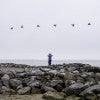 Jim Blackburn, a man in a blue shirt, stands on rocks and looks through binoculars on the Texas coastline 