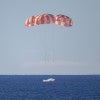 NASA's Orion spacecraft landing in the ocean: three striped parachutes landing on blue water