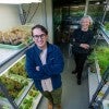 A young white man and older white woman stand in between shelves of plants