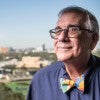 An older man with a colorful bowtie stares off into the distance, smiling 