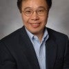 An Asian man in a suit smiles at the camera