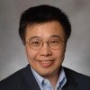 A Chinese man in glasses smiles at the camera 