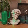 photo of objects with different reflectivity, including a gypsum bust, some shiny metallic figurines a plant, a green chest and green cactus-shaped vase, with green laser light shining across part of the image  