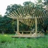 A wooden platform holds a picnic table with a leaf-shaped roof made of wooden slats 