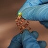 Stretchable moisture-activated battery held by two blue-gloved hands 