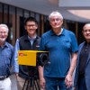 Four men stand outside around a yellow box.  