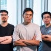 Three Asian men stand with their arms crossed in front of a window. 