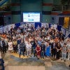 A large group of people stands in front of posters 