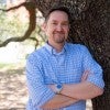 A while man stands in front of a tree and smiles 