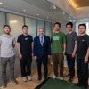 An older white man stands with five young Asian men.  