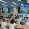 A speaker stands at a podium in a modern university lecture hall, presenting slides titled "Materials Science and NanoEngineering (MSNE)" on two large screens to an audience of university leaders and researchers seated at long wooden tables facing the front. 