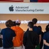 A group of students viewed from behind stands in front of a display at Apple’s Advanced Manufacturing Center, beneath a large wall sign featuring the Apple logo and center name. 